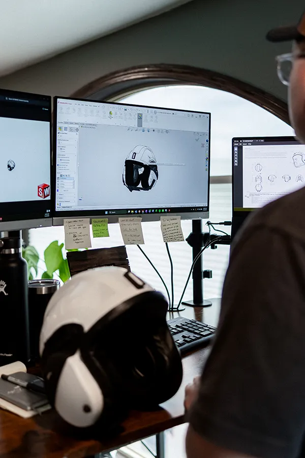 Engineer reviewing a helmet CAD model beside a physical prototype